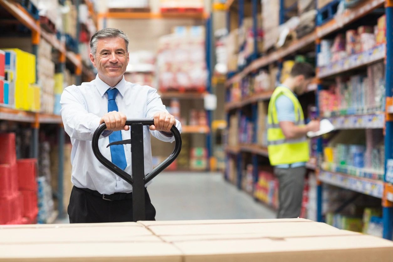 A man in a warehouse holding onto a hand truck.